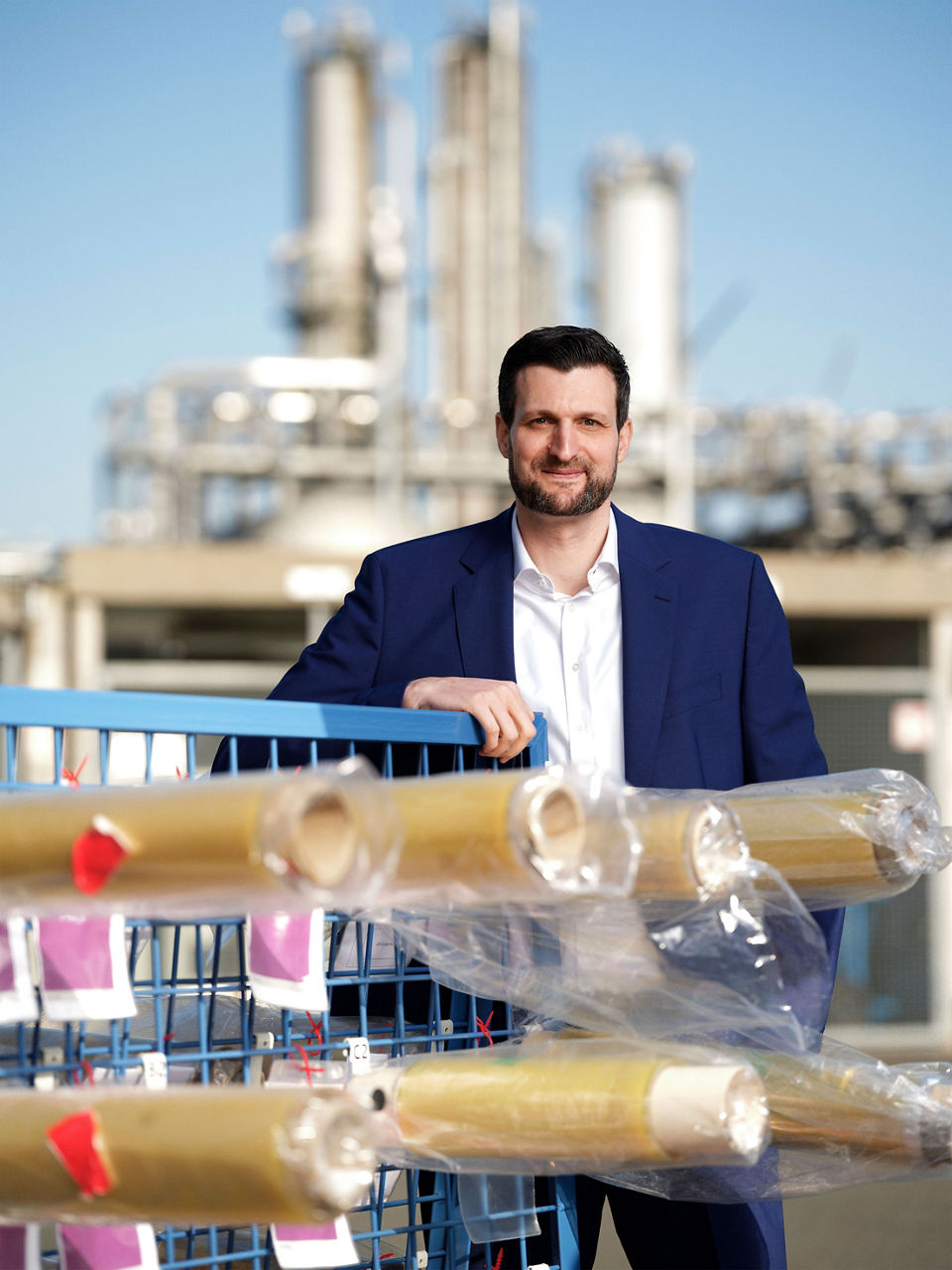 Christian Schnitzer steht hinter einem Transportwagen mit fertigen Membranrollen. Im Hintergrund ist der Chemiepark Marl zu sehen.