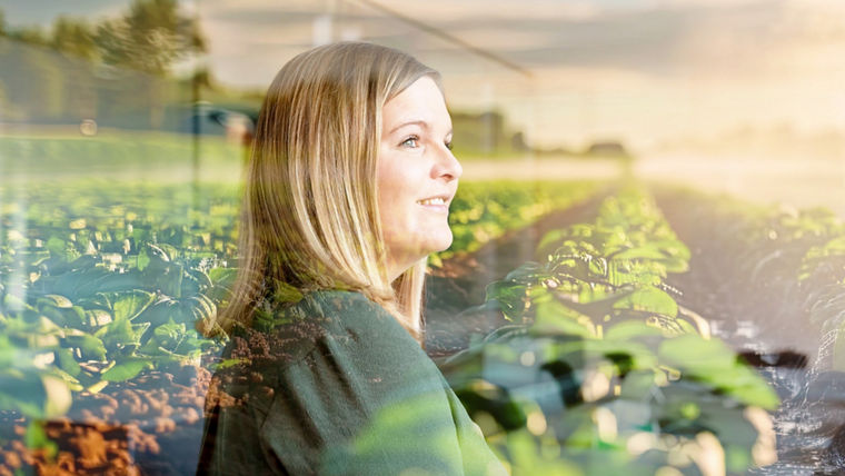 A female Evonik employee is standing in front of an agricultural field and looking to the right with a smile.