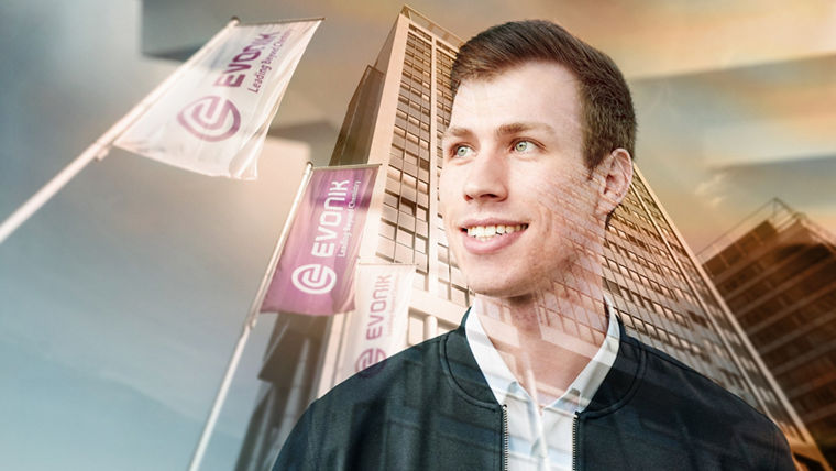 A young Evonik employee is standing in front of the Evonik headquarters and looking to the left with a smile.