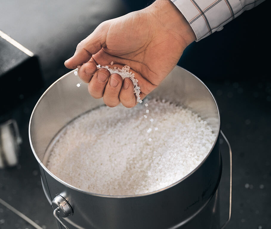 A hand checks white plastic granulate.