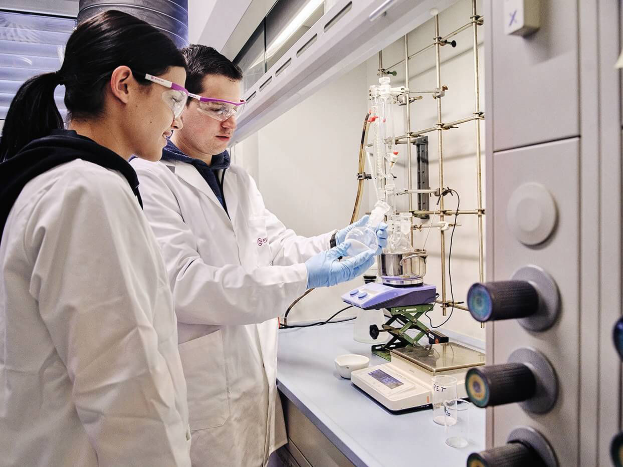 Zwei Mitarbeitende des Labors entnehmen etwas aus einem Glaskolben.