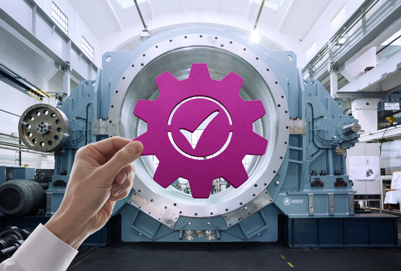 Hand holding a purple gear icon with a checkmark inside, positioned in front of industrial machinery.