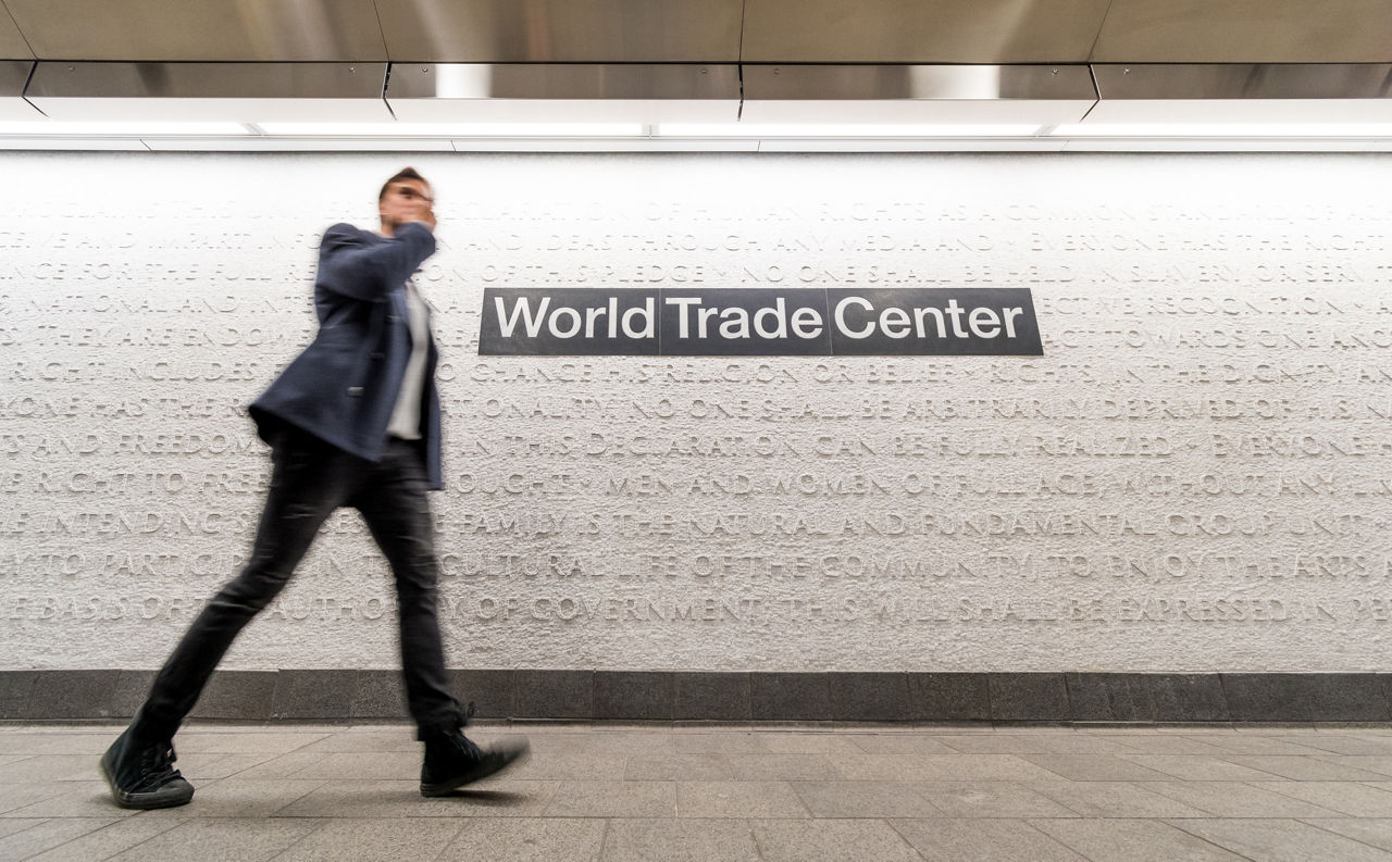 A man walks past the marble mosaic in Cortland Station. On the wall is the station sign “World Trade Center”.