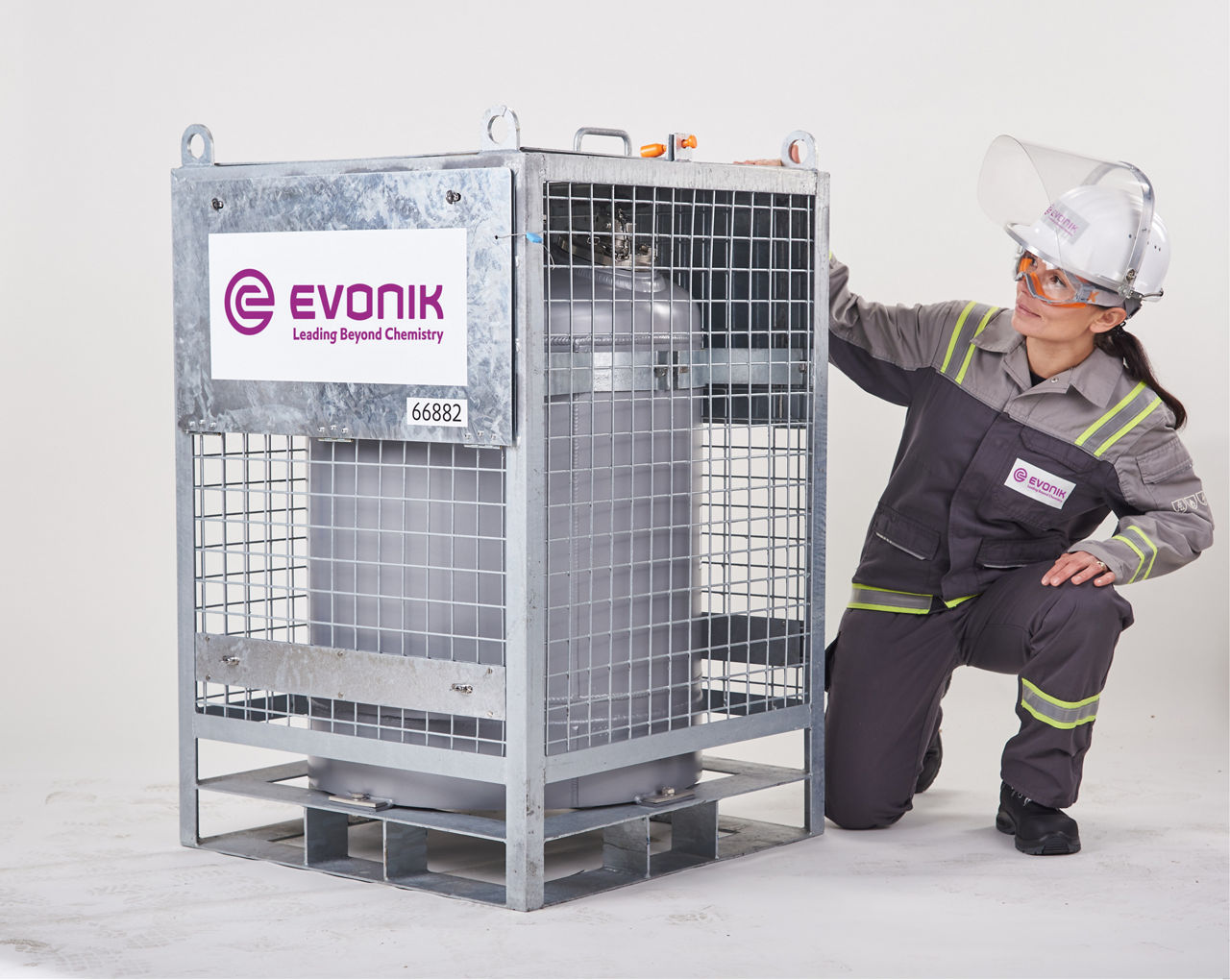 Eine Evonik-Mitarbeiterin überprüft einen Transportbehälter, der zusätzlich von einem Gitterkasten umhüllt ist.