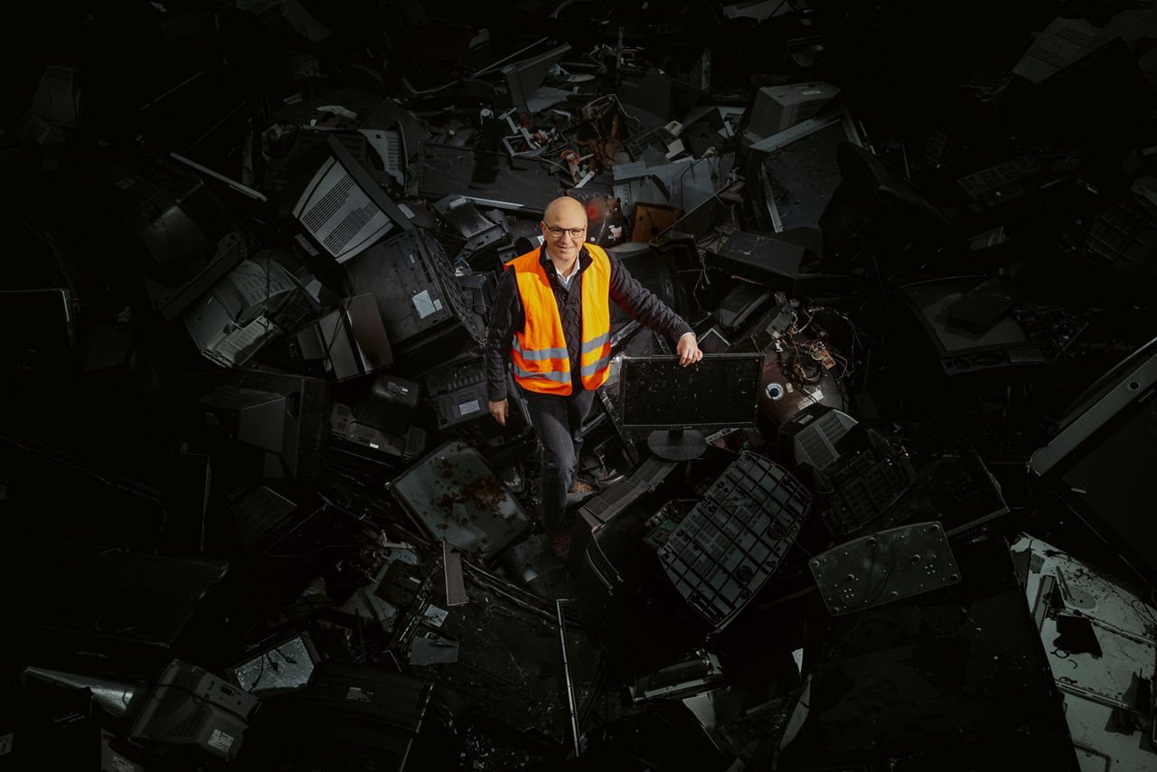 Daniel Goldmann is standing on a stockpile of electronic scrap, mostly monitors, wearing a safety vest.