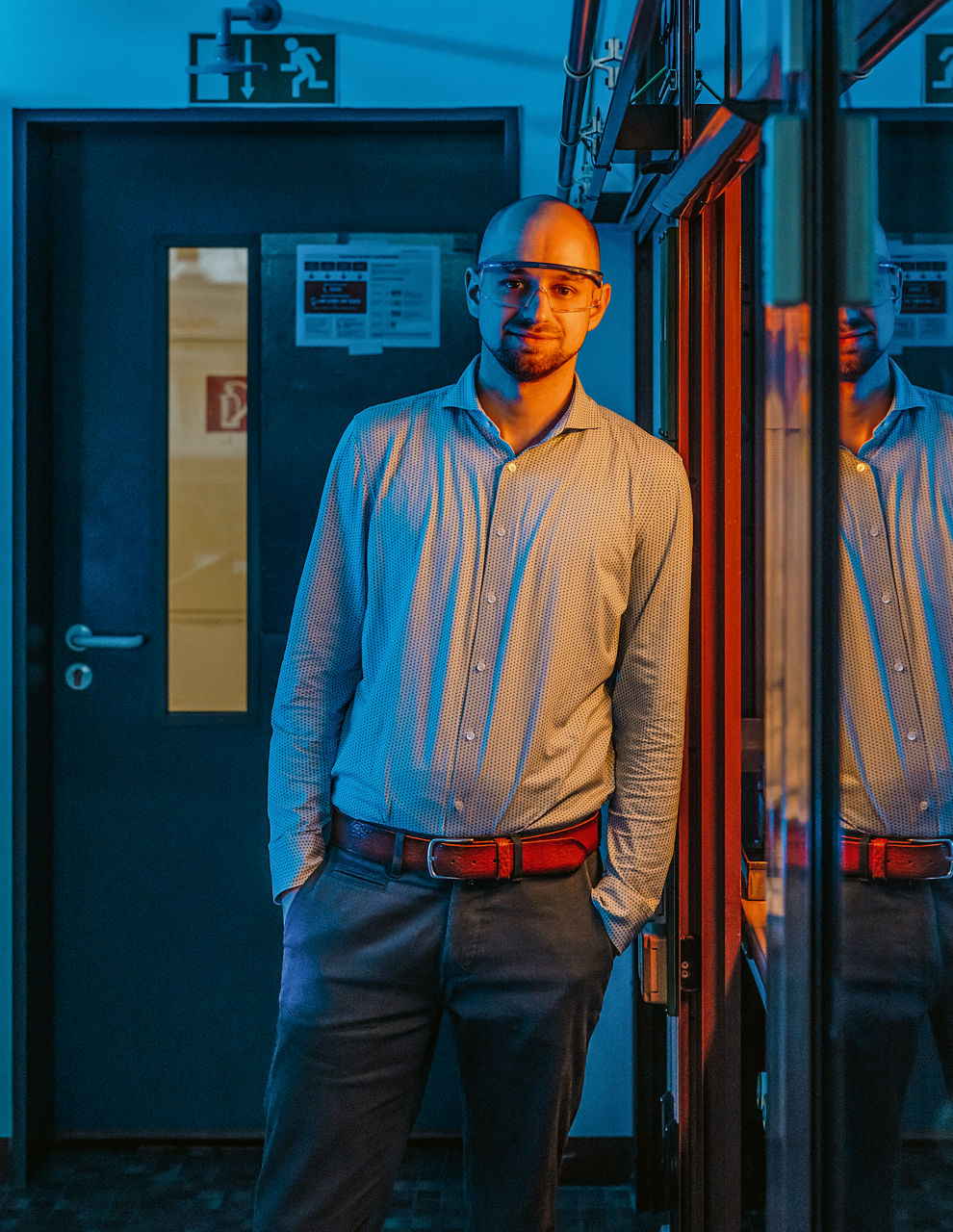 Hendrik Rehage lehnt stehend am Schrank mit dem Versuchsaufbau. Der schaut in die kamera und hat die Hände in den Hosentaschen. Er trägt eine Schutzbrille.
