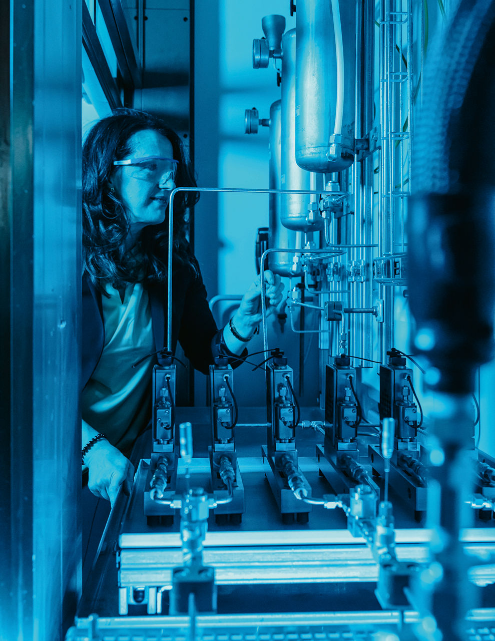 Senada Schaack prüft die Apparatur, die in einem Behälter montiert ist. Sie trägt eine Schutzbrille, der Raum ist blau beleuchtet.