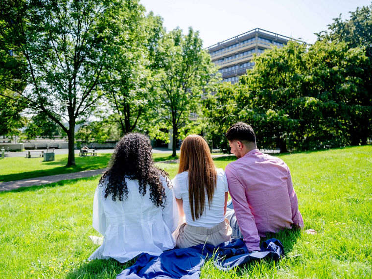 Drei Studierende sitzen auf einer grünen Wiese auf dem Campus der Ruhr-Universität.