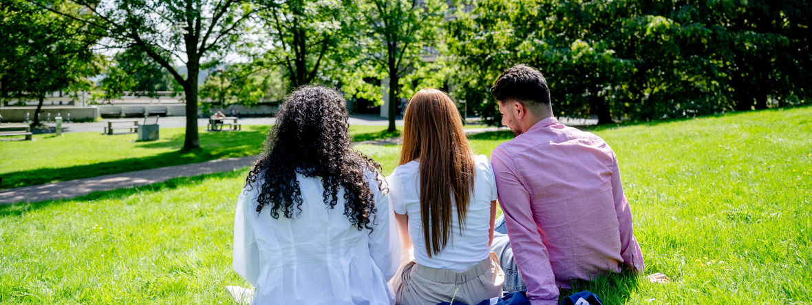 Drei Studierende sitzen auf einer grünen Wiese auf dem Campus der Ruhr-Universität.