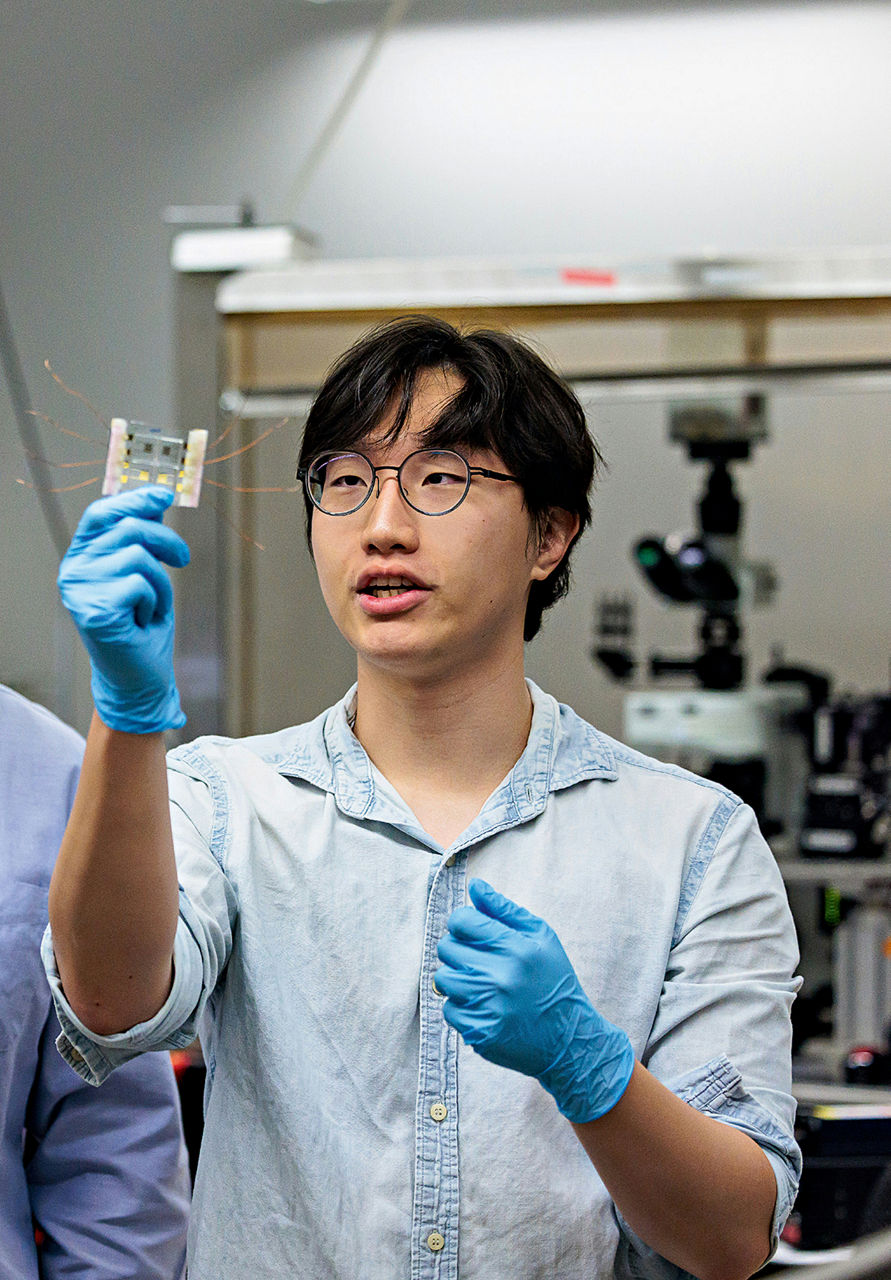 Saeyhun Kim looks at a chip with wires coming out of it.