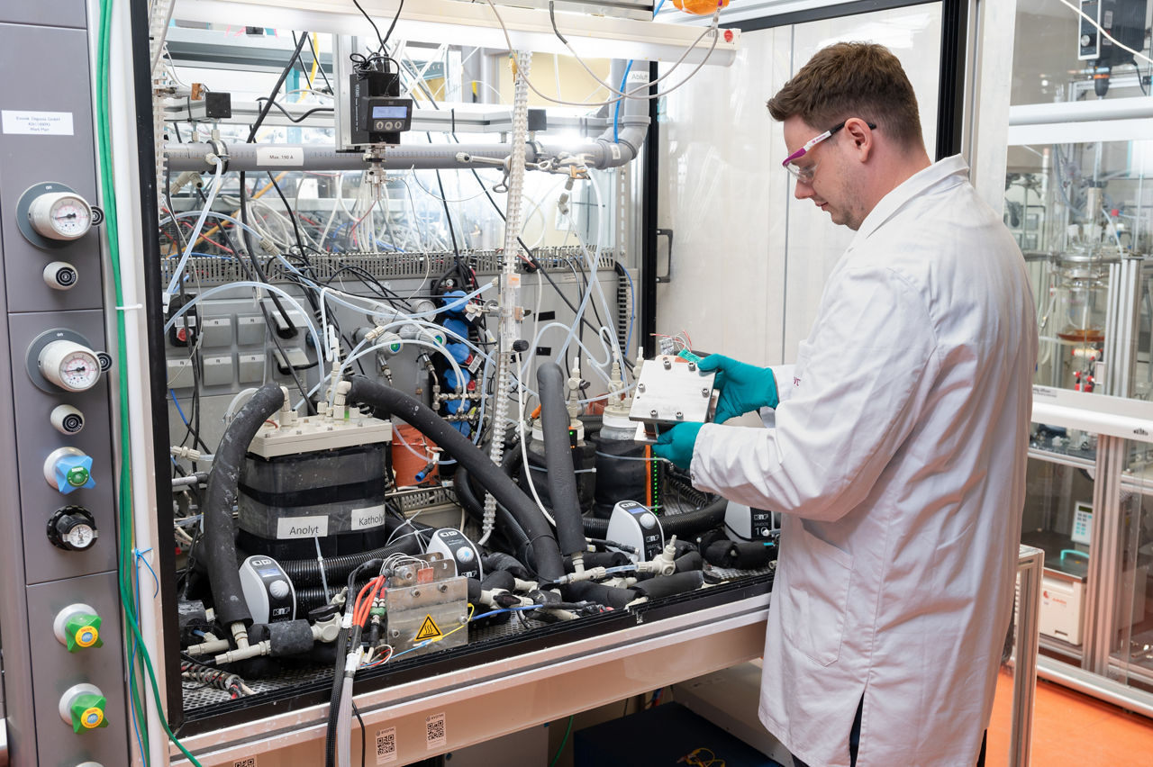 Philipp Roters vor einem Versuchsschrank mit zahlreichen Kontrollschaltern, Kabeln und Schläuchen.