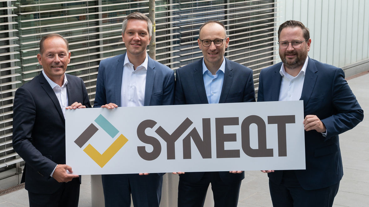 SNYEQT-Geschäftsführung mit Evonik-Personalvorstand Thomas Wessel (v.l.): Andreas Orwat, Thomas Basten und Daniel Brünink. Sie halten ein großes Schild mit dem Logo von SYNEQT. 