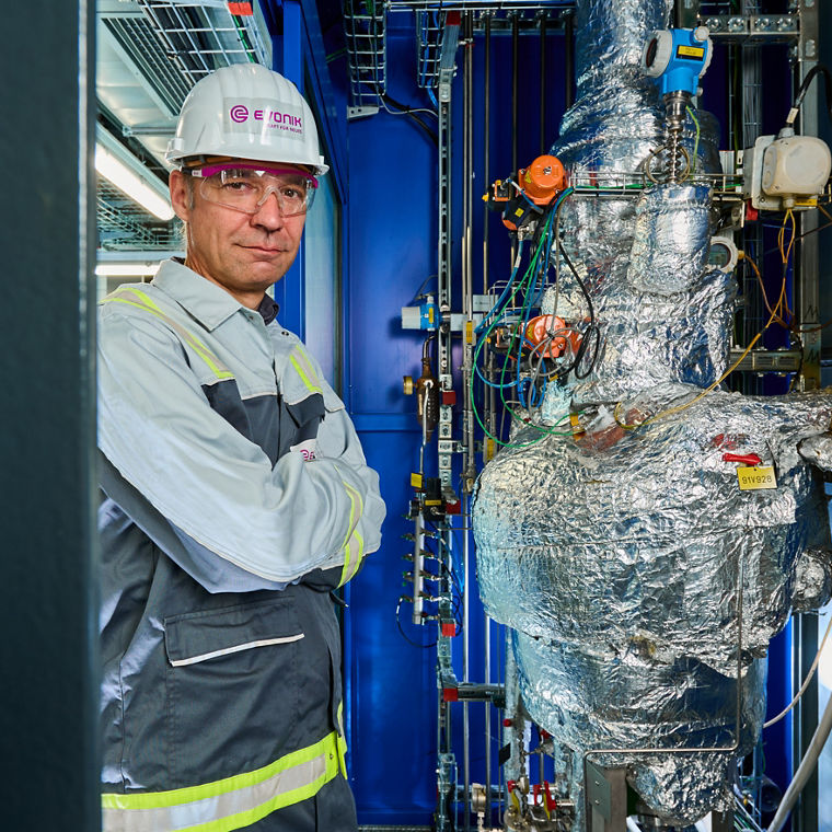 Worker in protective gear standing next to a large industrial machine wrapped in insulation material.