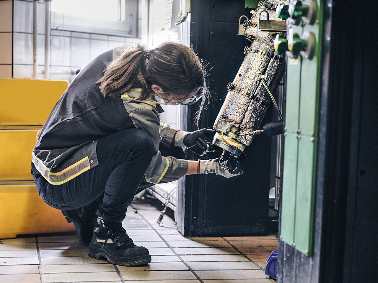 Eine Frau in Arbeitskleidung sitzt in der Hocke und montiert etwas an der Anlage.