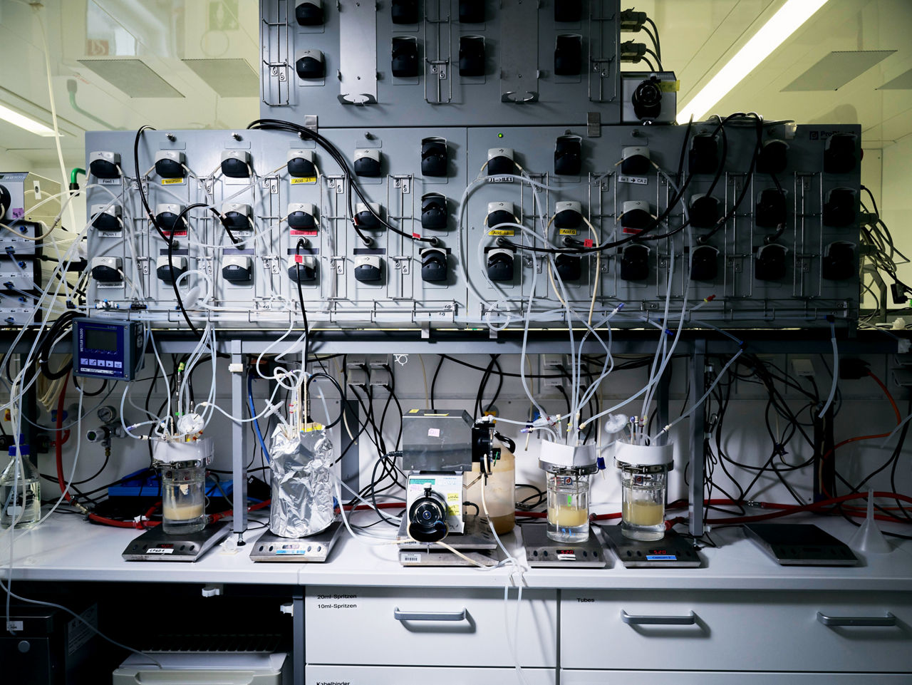 A laboratory cabinet with various glass containers in front, connected by numerous tubes.
