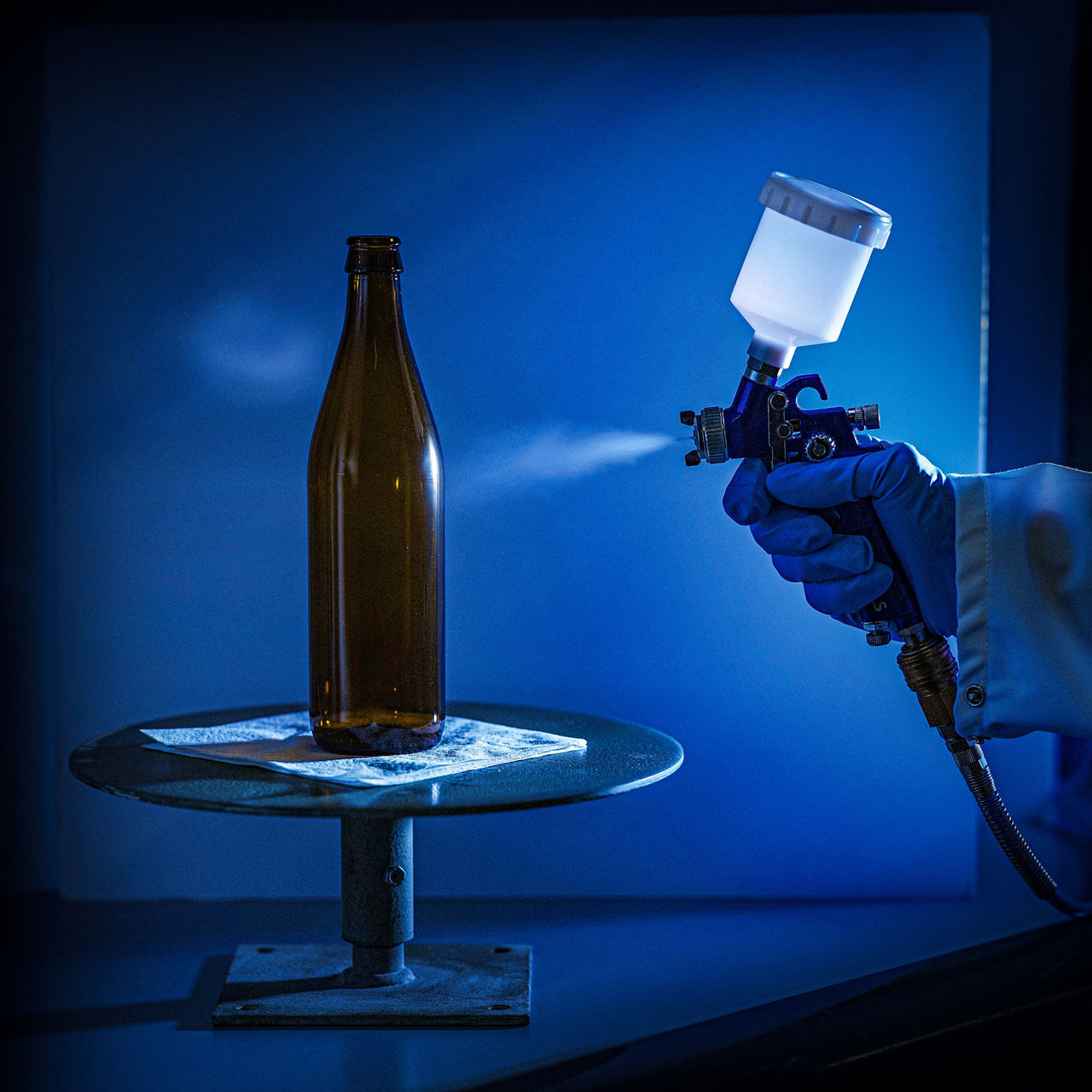 Eine braune Getränkeflasche wird aus einer Spritzpistole mit feinem Nebel besprüht.