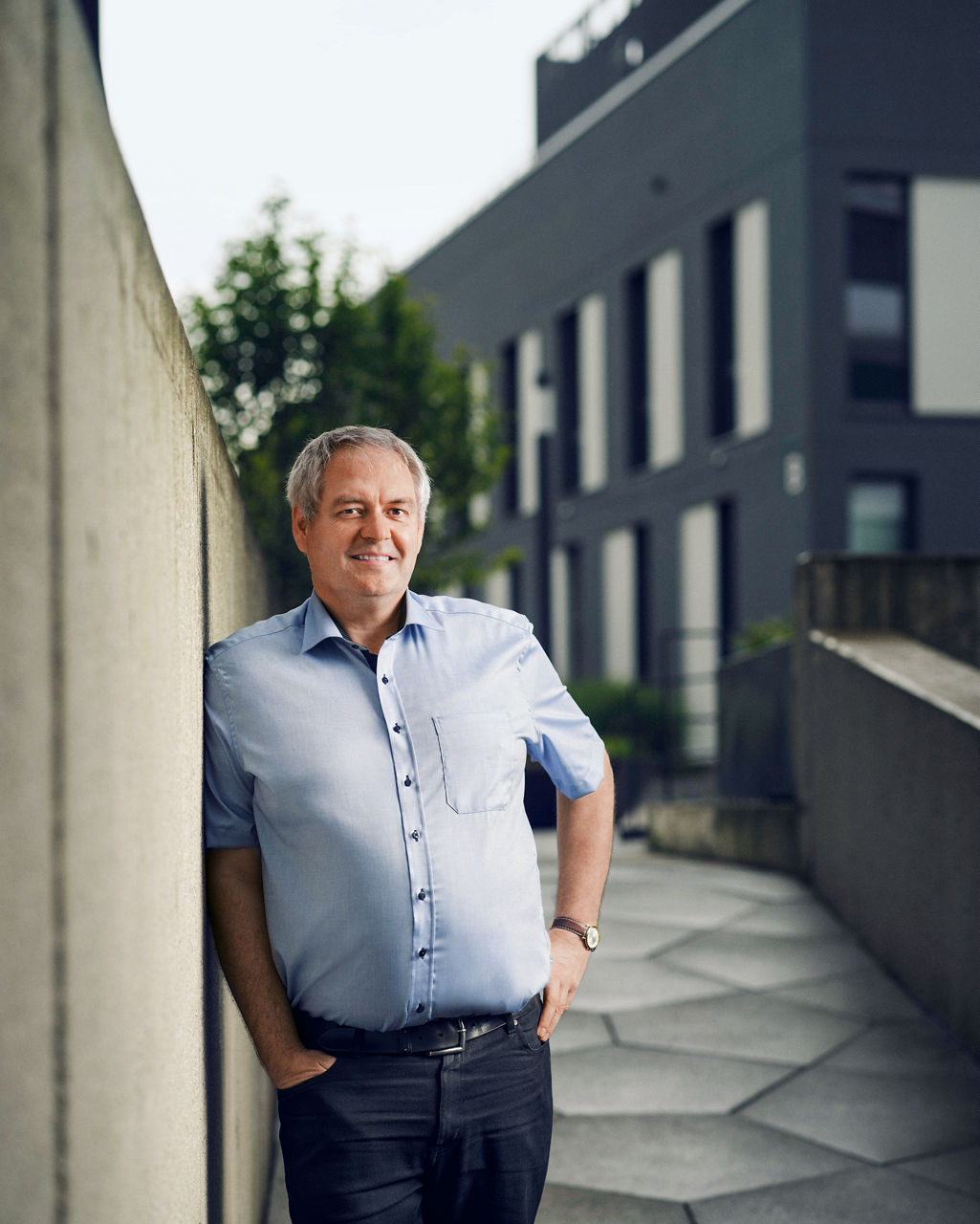 Siegried Waldvogel lehnt an einer Außenwand und lächelt in die Kamera.