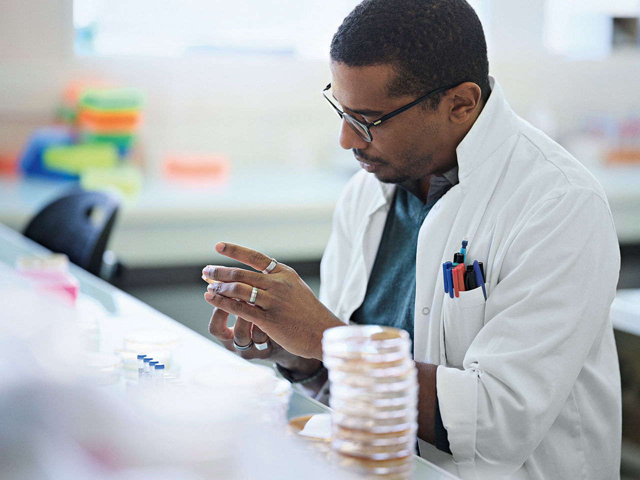 Ein Wissenschaftler in weißem Laborjittel betrachtet eine Petrischale mit einer Probe.