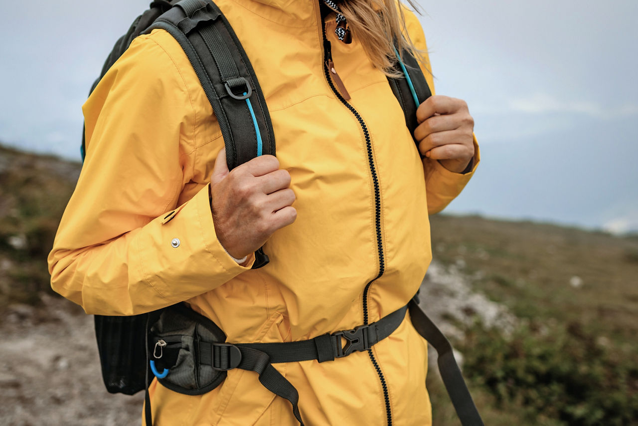 Waterproof warm clothing for extreme weather. Woman hiking in mountains and wearing yellow raincoat