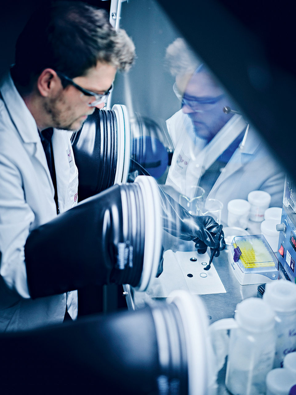 Frank Löffler greift durch eine Handschuhschleuse in einen Reinraum-Schrank um die Knopfzelle zu befüllen.