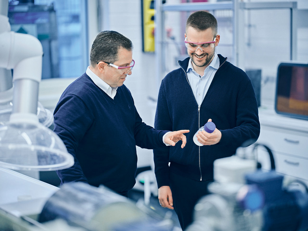hristos Sarigiannidis und Jan Blankenburg betrachten gemeinsam in einem Labor ein transparentes Probenfläschchen.