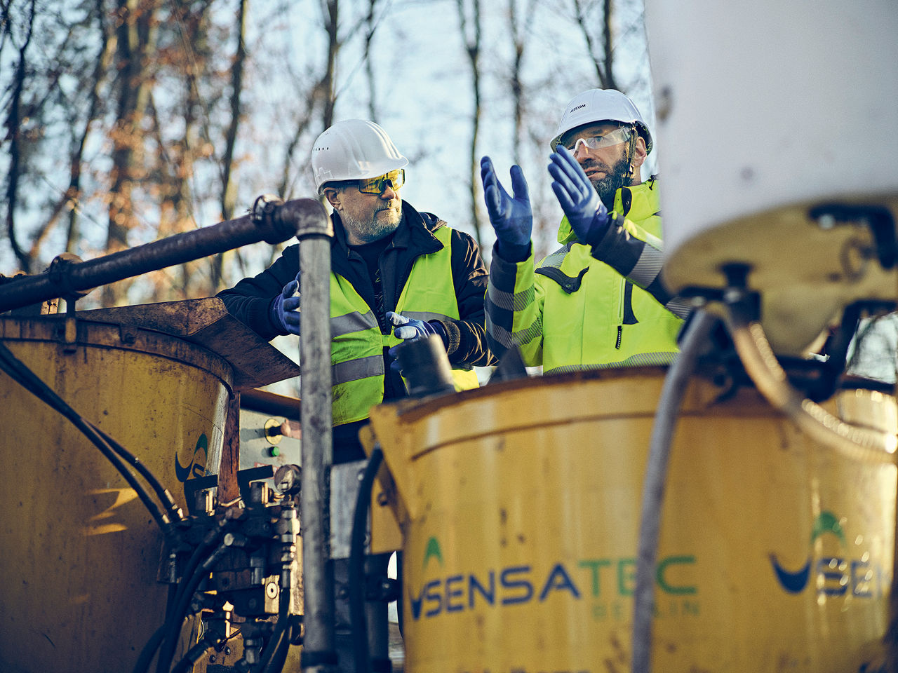 Two employees stand behind a mixing machine outdoors