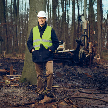 Gordon Bures lehnt in Arbeitskleidung an einem Baum.