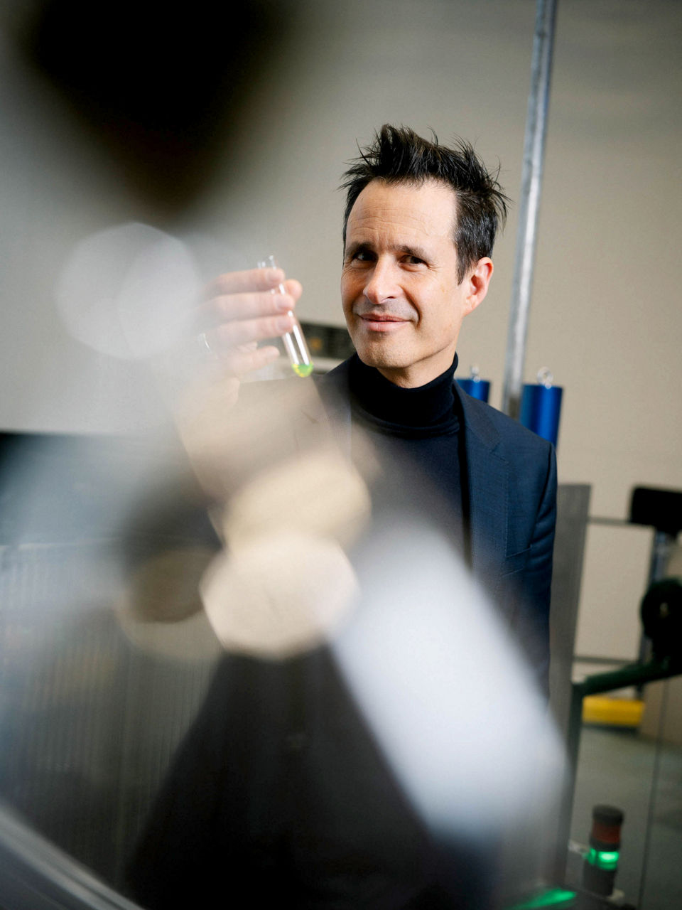 Thorsten Schumm hält ein Reagenzglas mit einer winzigen Menge grüner Flüssigkeit in der Hand.