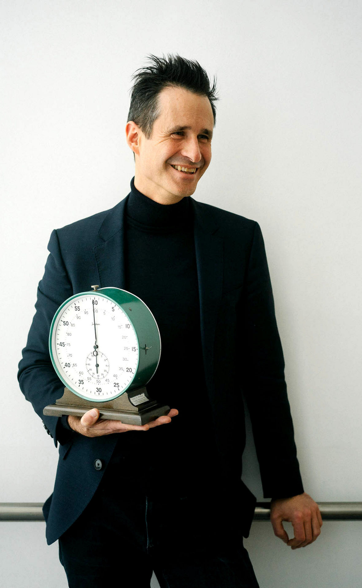 Thorsten Schumm hält eine große analoge Stoppuhr auf der rechten Hand und lacht.