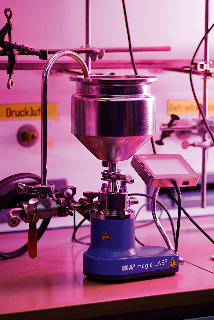 Ein Metallbehälter in einer Halterung, von oben führt ein gebogenes Rohr hinein.