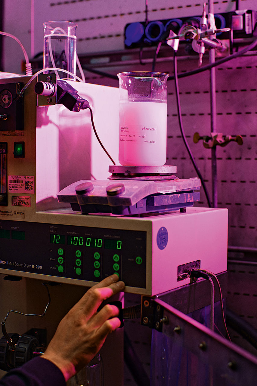 Ein Messbehälter auf einem Messgerät. Im Kolben eine weißliche Flüssigkeit, eine Hand stellt am Gerät Werte ein.