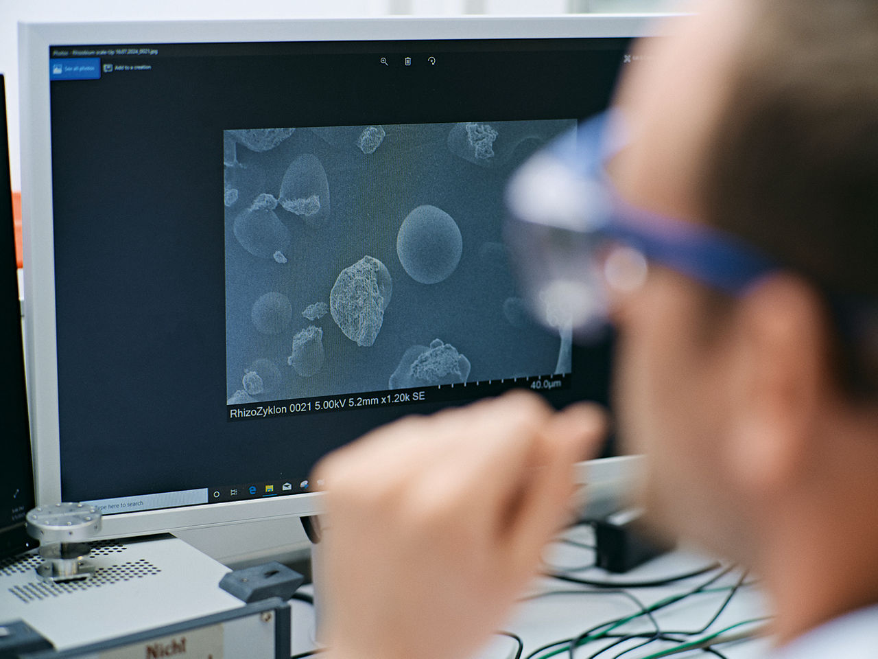 Max Brauns Kopf von seitlich hinten. Er schaut auf einen Monitor mit Mikroskopaufnahmen.