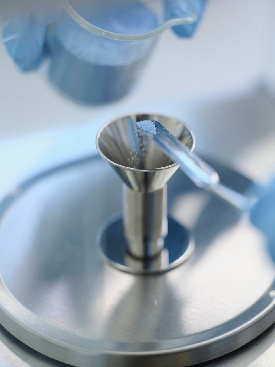 Eine Hand füllt vorsichtig etwas blaues Pulver in einen kleinen Edelstahltrichter.