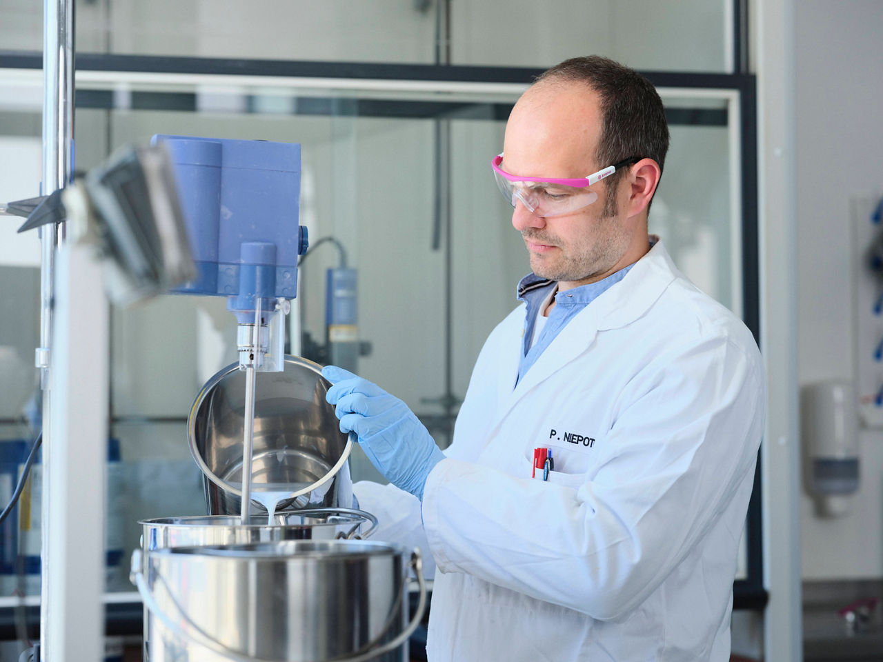 Peter Niepoth schütteet vorsichtig eine weiße Flüssigkeit aus einem Edelstahlbehälter in ein Rührwerk vor ihm.