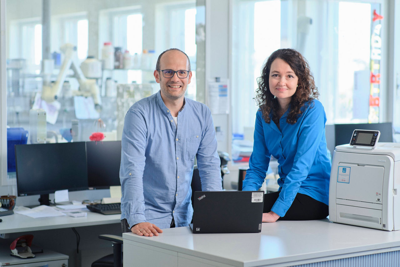 Peter Niepoth und Dr. Bettina Hölzer stehen gemeinsam hinter einem Laptop und lächeln in die Kamera-