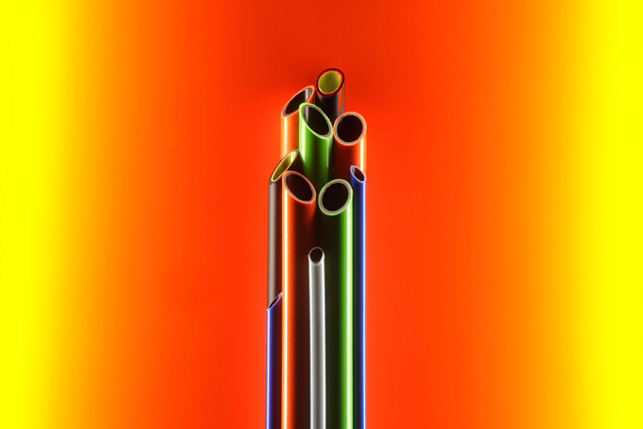 Multicolored, vertically standing pipes against an orange-yellow background.