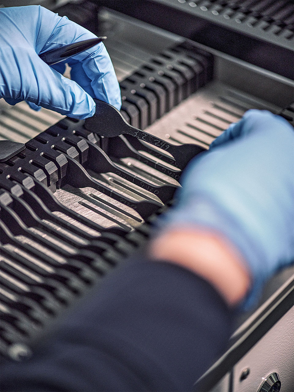 Zwei Hände in blauen Handschuhen entnehmen ein Prüfstück aus einer Halterung.