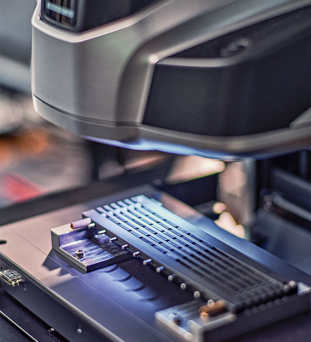 Ein Gummistreifen liegt in einem Testgerät und wird mit bläulichem Licht angestrahlt.