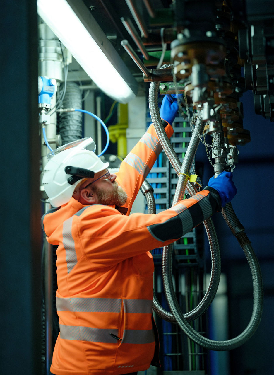 Chemikant André Schumacher in orangefarbener Jacke mit Helm und Handschuhen kontrolliert die Anlage.