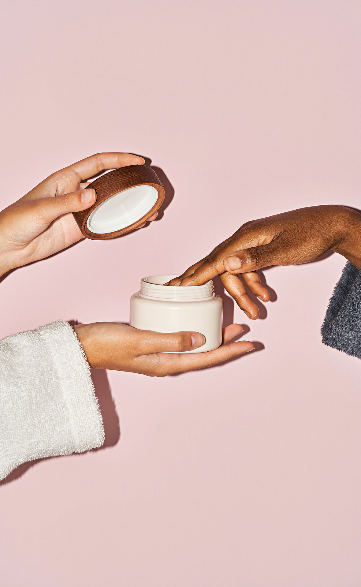 Zwei Frauenhände öffnen von links einen Creme-Tiegel. Eine Frauenhand nimmt von rechts mit einem Finger etwas aus dem Tiegel.