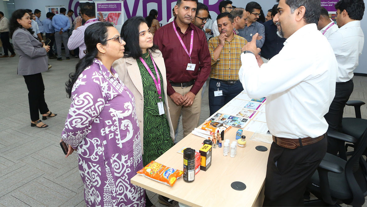 A group of professionals engaged in discussion at an event, with a table displaying various products.