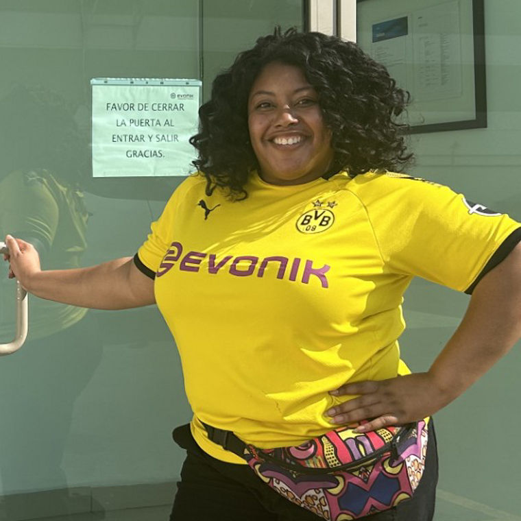 Woman in a yellow shirt standing by a glass door with "220-22 Bodega 36" written above it.