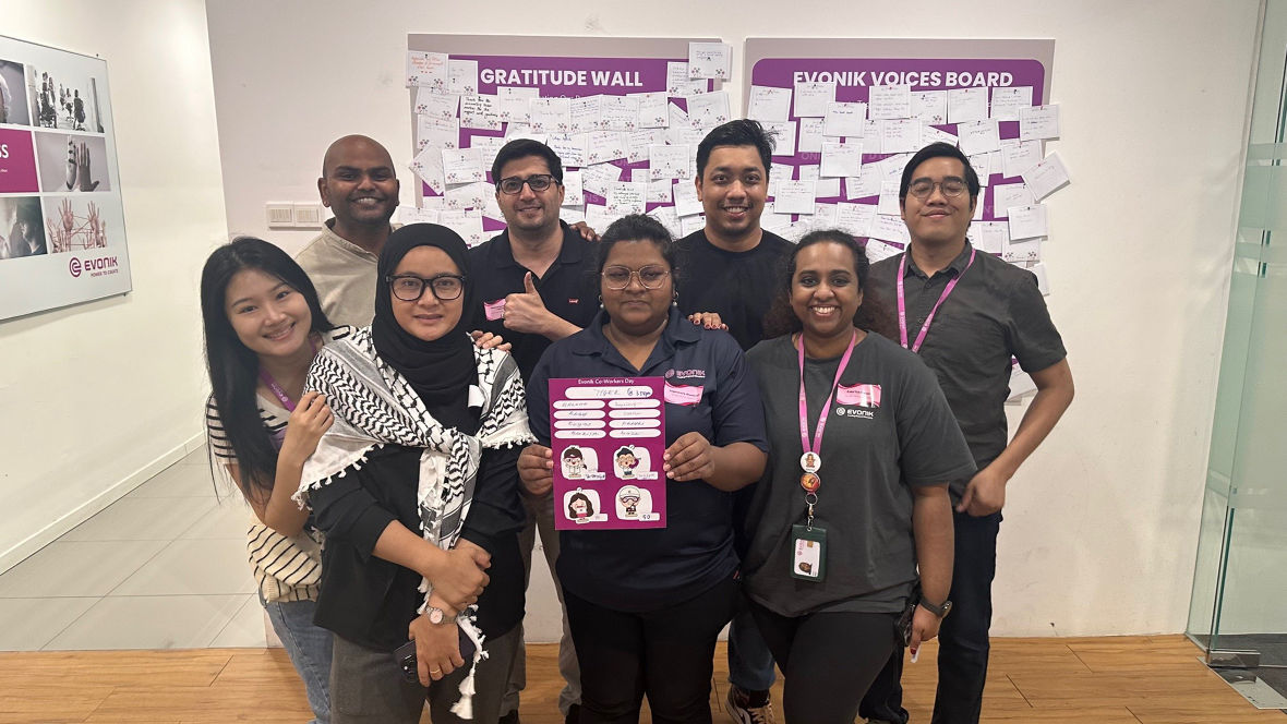 Group of coworkers posing in front of a gratitude wall and an Evonik voices board during a company event.