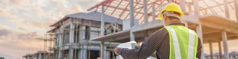 Professional engineer architect worker with protective helmet and blueprints paper at house building construction site background
