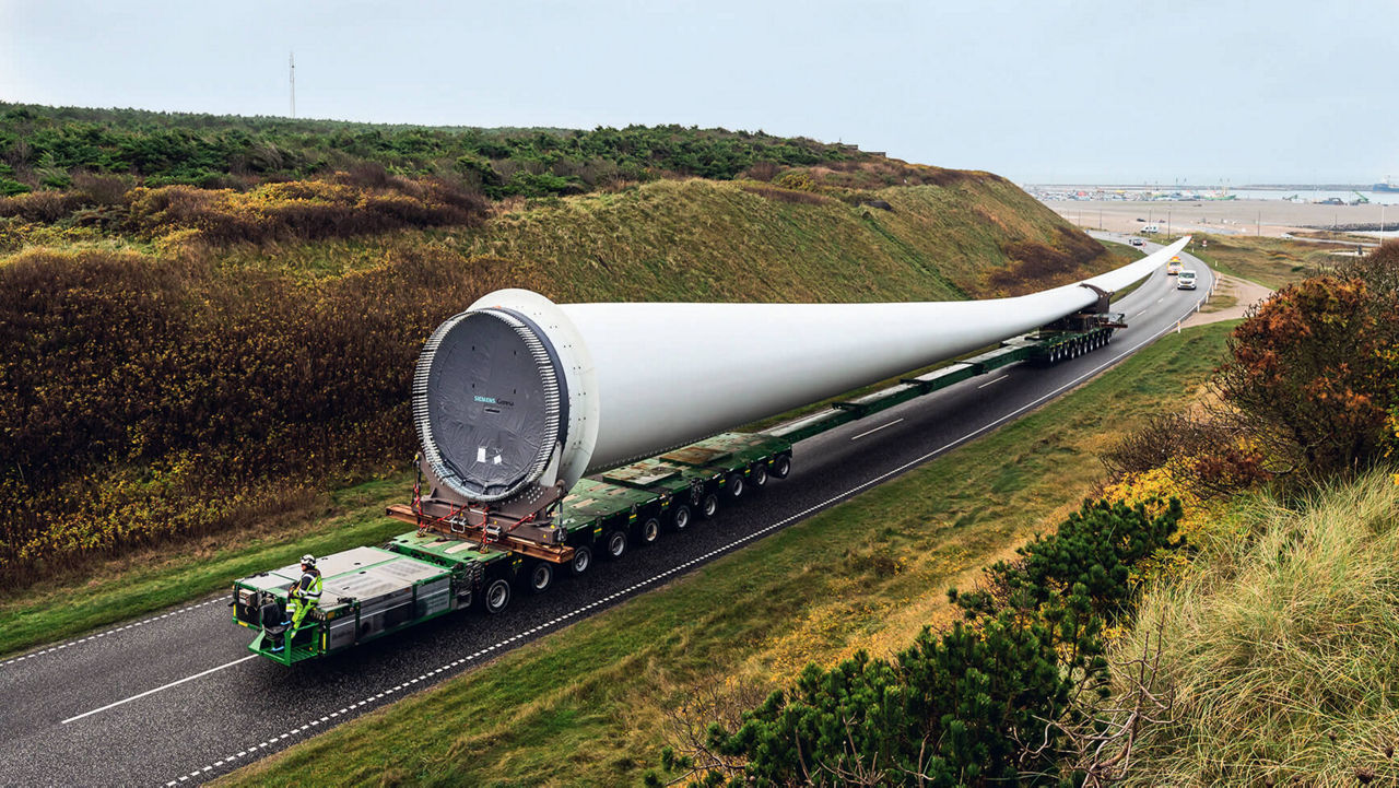 A heavy goods vehicle with a huge rotor blade on a coastal road.