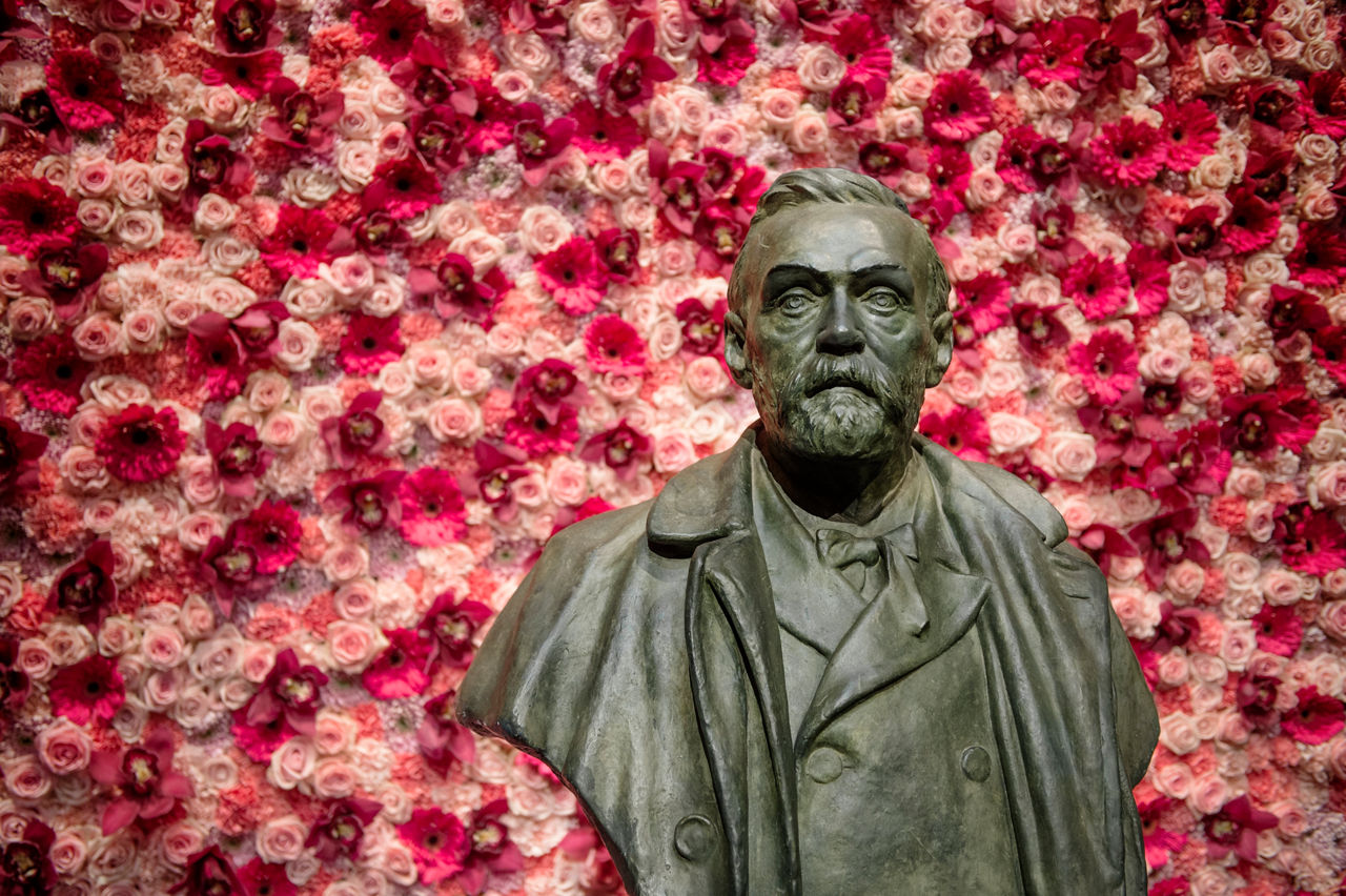 Ein Bronze-Büste von Alfred Nobel vor einer Wand mit roten Blumen