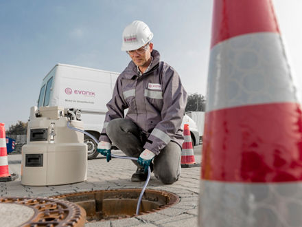 Ein Evonik-Mitarbeiter entnimmt eine Probe Wasser aus einem Abwasserschacht.
