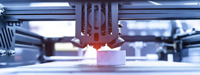 A close-up view of a 3D printer in action, producing a white polymer component using advanced additive manufacturing technology. The image highlights the precision and industrial setup of the printing process.