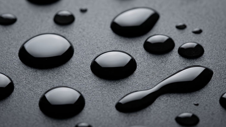 Glossy black liquid droplets of various sizes on a textured dark surface.
