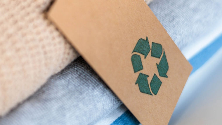 Knitted warm clothes neatly folded heap with craft tag recycling material circle arrow closeup. Eco friendly fashion clothing laundry garment made by recycled zero waste renewable textile technology